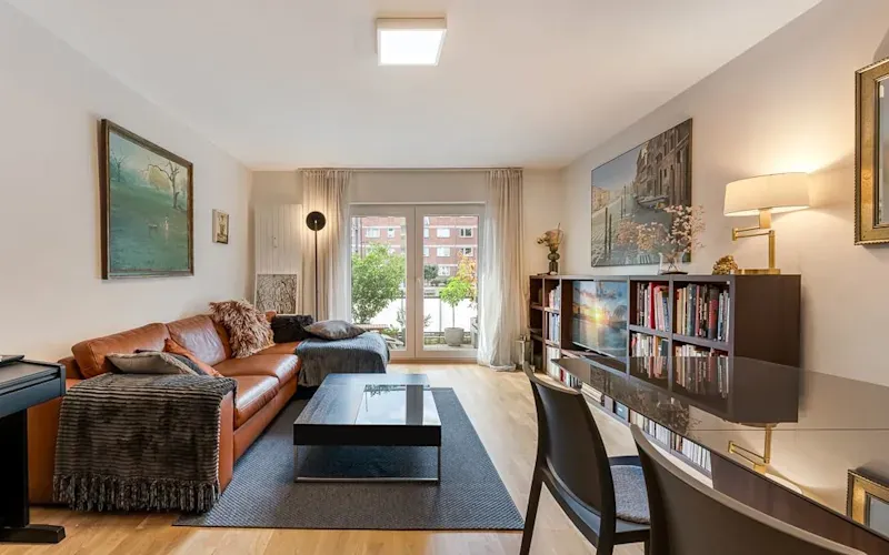 Modernes Wohnzimmer mit Ledersofa, großem Fenster, Bücherregal und Esstisch.