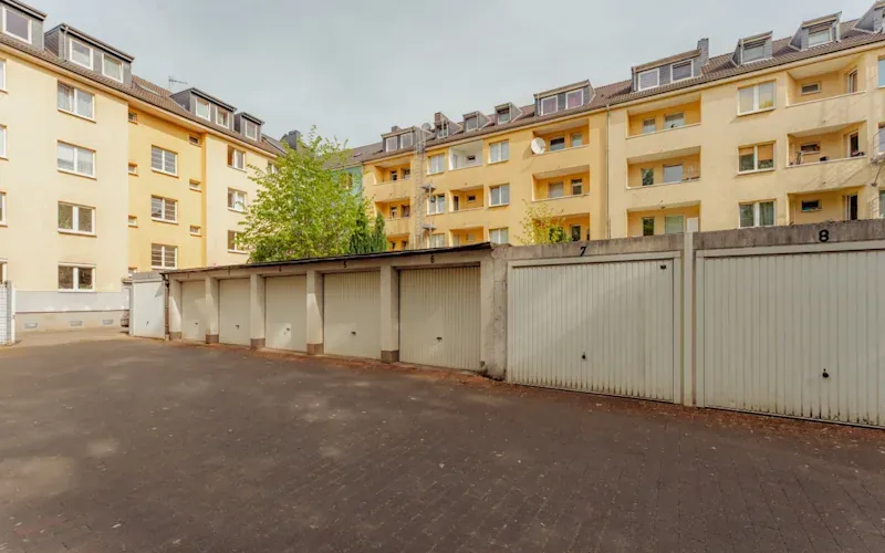 Mehrere verschlossene Garagentore vor einem gelben Mehrfamilienhaus mit Balkonen.