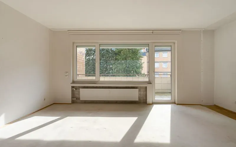 Leeres, helles Zimmer mit großem Fenster, Heizung und Zugang zu einem Balkon.