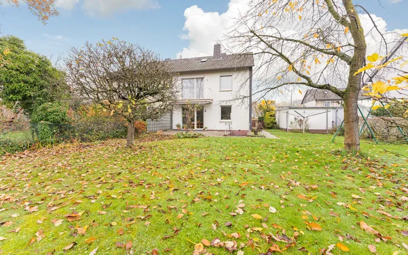 Zweistöckiges Wohnhaus mit großem Garten und herbstlich bedecktem Rasen.