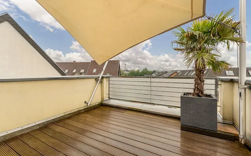 Balkon mit Holzfußboden, Sonnensegel und Palme im großen Pflanzkübel.
