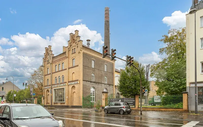 Altes Backsteingebäude mit Turm und Schornstein an einer nassen Straßenkreuzung.