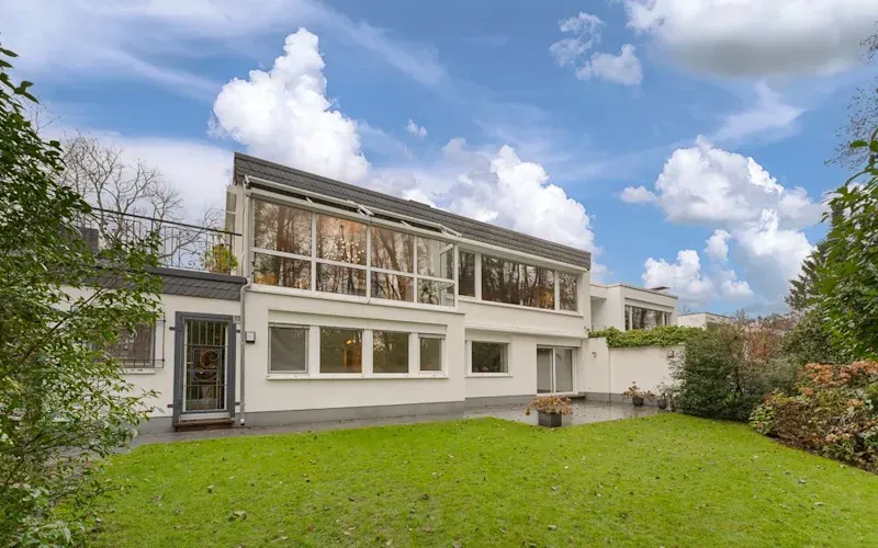 Moderne weiße Wohnhausfassade mit großen Fenstern und Garten bei Tageslicht.