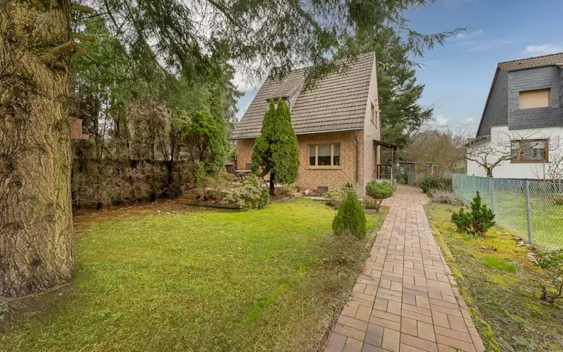 Gepflegter Garten mit Gehweg führt zu einem Einfamilienhaus mit Satteldach.
