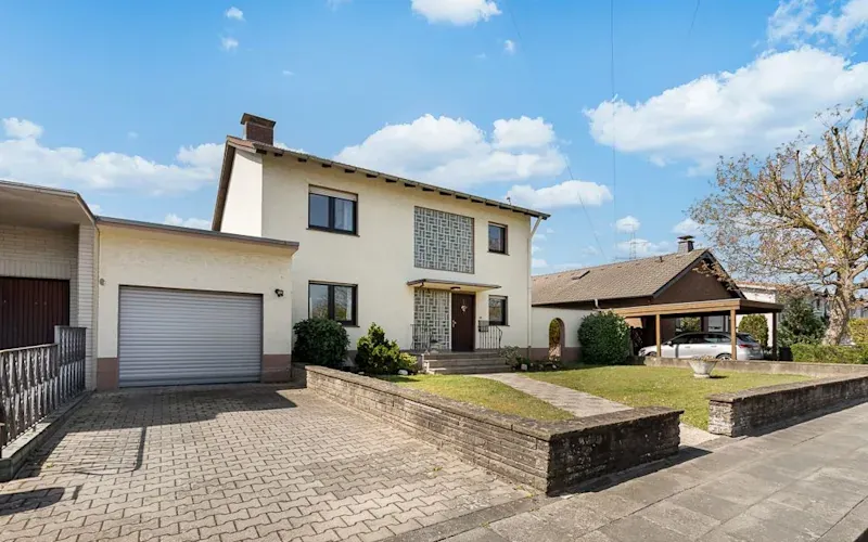 Zweistöckiges Wohnhaus mit Garage, Auffahrt und Vorgarten an einem sonnigen Tag.
