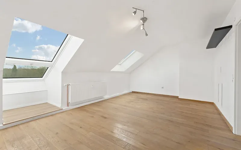 Heller Dachraum mit Holzfußboden, weißen Wänden und großen Dachfenstern.