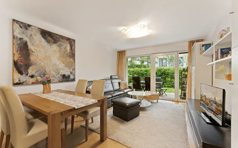 Modernes Wohnzimmer mit Esstisch, Sofa, TV, großem Gemälde und Zugang zur Terrasse mit Gartenblick.